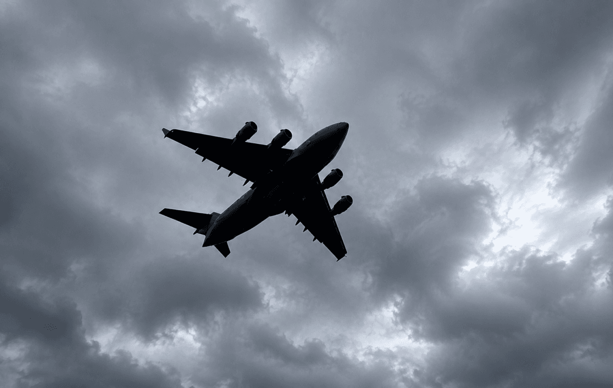 Avião de grande porte visto de baixo sob nuvens escuras em frame real aprimorado e expandido com IA.