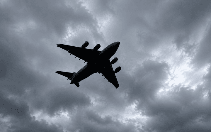 Avião de grande porte visto de baixo sob nuvens escuras em frame real aprimorado e expandido com IA.