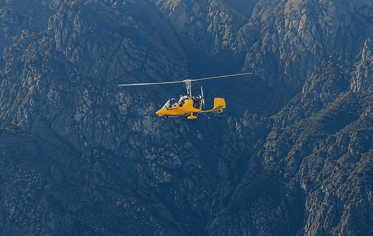 Autogiro amarelo com dois ocupantes sobrevoa região montanhosa no norte da Itália.