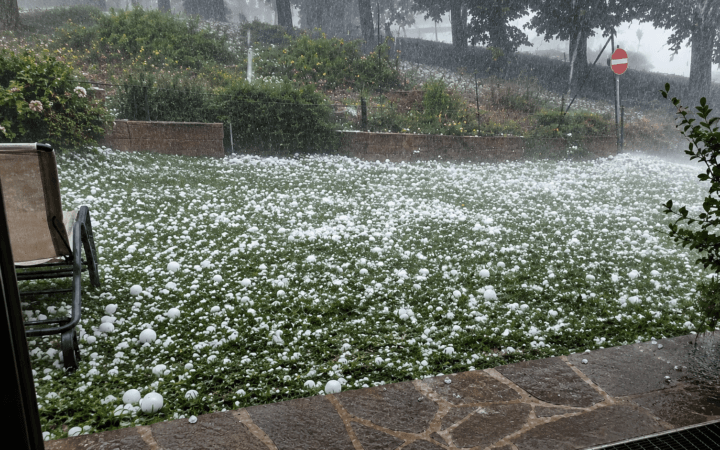 Frame real aprimorado por IA mostra forte chuva de granizo cobrindo um gramado com pedras de gelo.