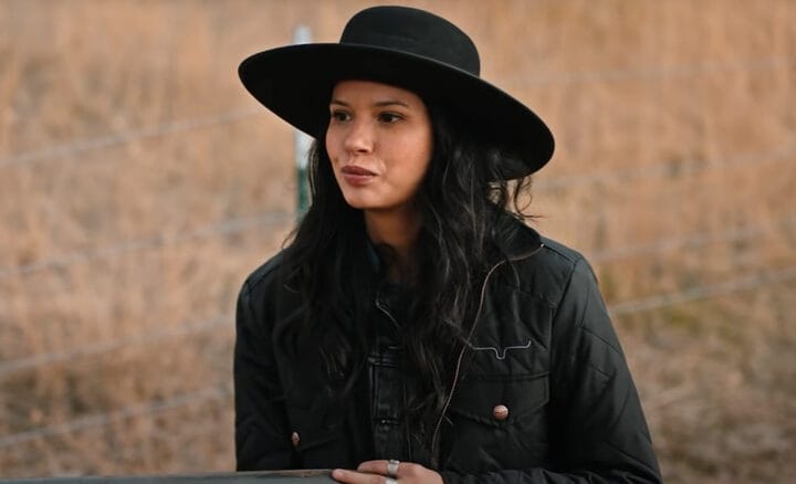 Personagem aparece com chapéu preto em frame real de Yellowstone, em cenário rural característico da série.
