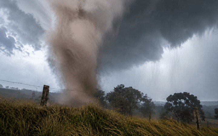 Ilustração por IA mostra tornado tocando o solo em área rural sob uma grande tempestade e cortinas de chuva.